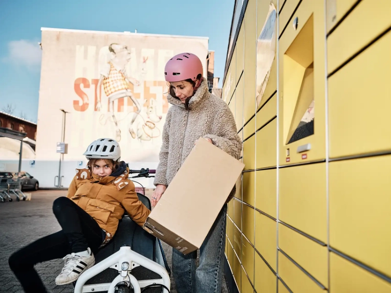 Frau mit Kind und Lastenrad holt Paket an Packstation ab